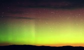 Green, yellow and red aurora borealis above a silhouette of rolling hills