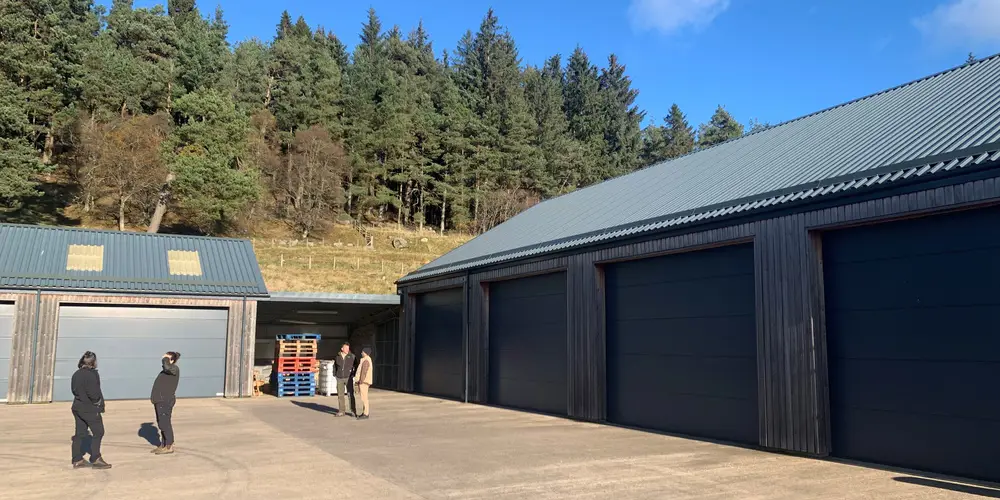 Four L shaped garage doors with people standing in front of them and forest behind