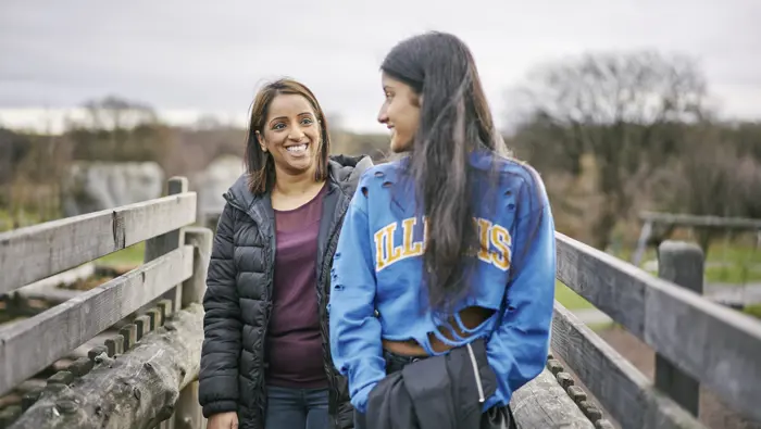 Smiling young woman and teenage girl walk across wooden bridge in Cuningar Loop Woodland Park, Glasgow