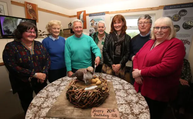 A group of people slice a cake shaped like an osprey nest