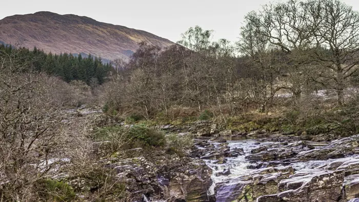 Waterfall in the foreground with trees and a hill in the background.