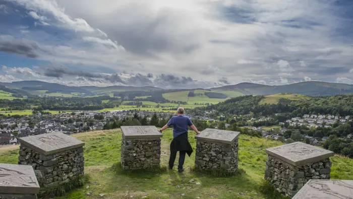 Person standing at a viewpoint next to sculpture plinths.