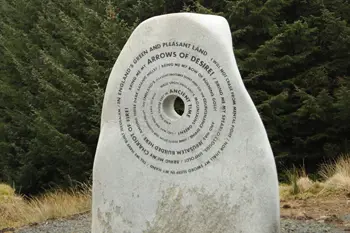 A large boulder sits in front of a woodland, boulder has inscription circling around a large carved hole