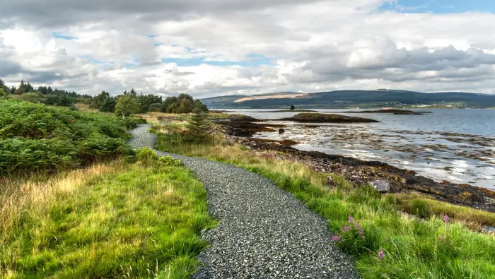 : A gravel path next to the sea with an island