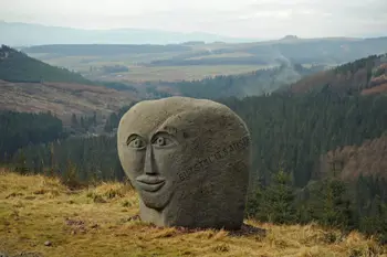 A large boulder on the hillside with a face carved into it.