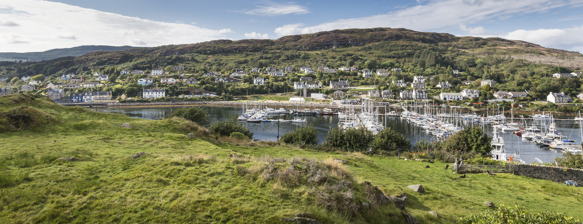 Aerial view over a boat filled harbour and small coastal town with hills in the background