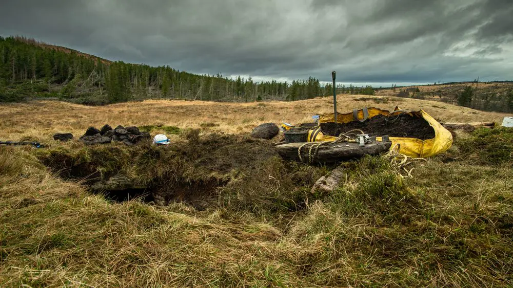 A hole in the ground with a yellow bag of mud next to it and a shovel 