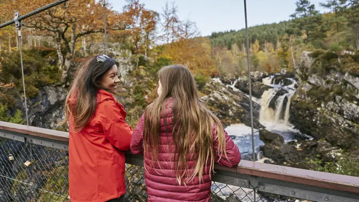 Two people on a bridge next to a waterfall.