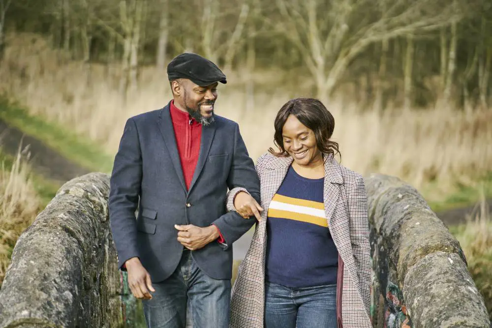 A man and woman smiling and walking together over a narrow stone humpback bridge