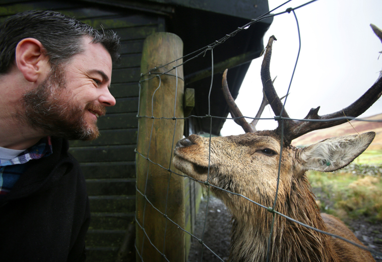 A male visitor stands close to a wire fence with a stag deer standing across from him