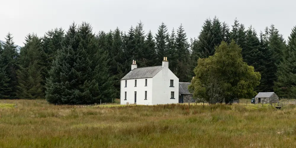 A two store white stone building with trees behind it