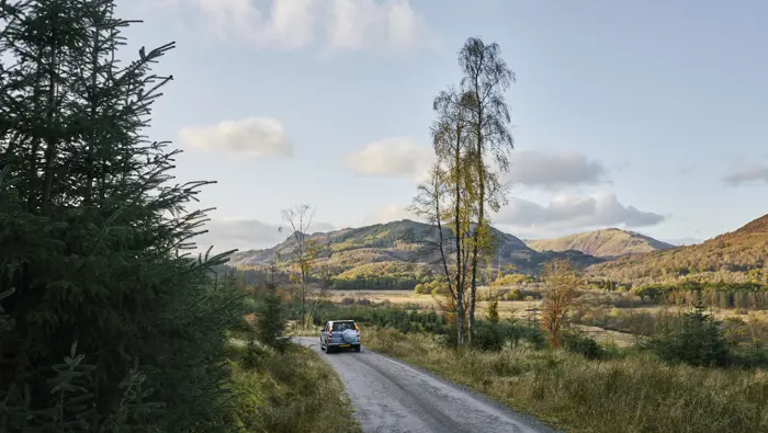 A car on a forest road with trees and hills in the background.