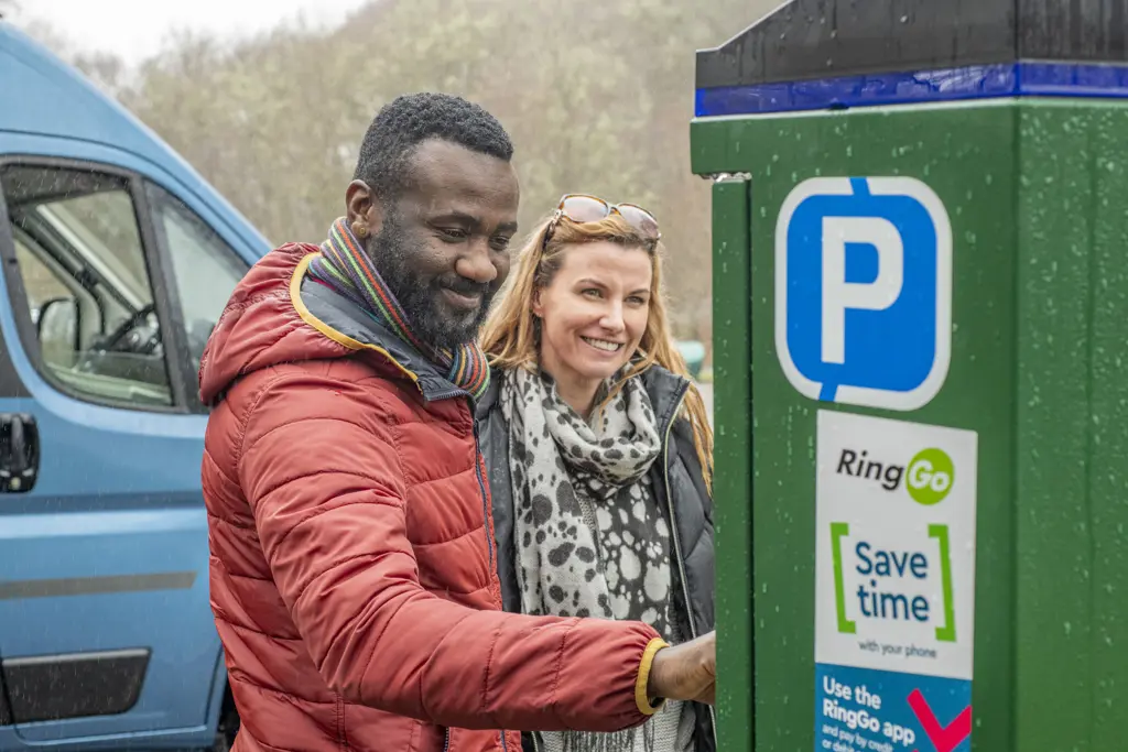 couple using a parking meter with the RingGo logo, in front of a blue motorhome/campervan.