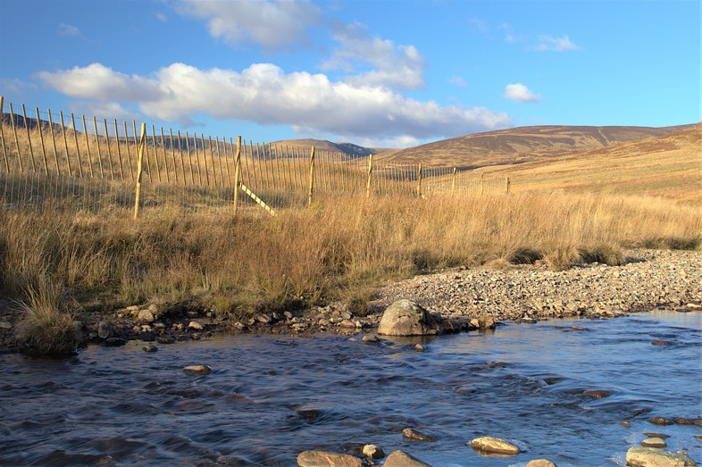 A wooden fence next to water with hills behind