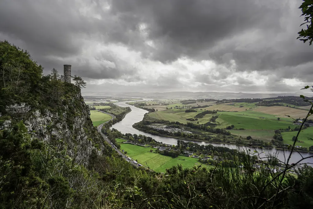 A cliff with a tower overlooking a river surrounded by fields.
