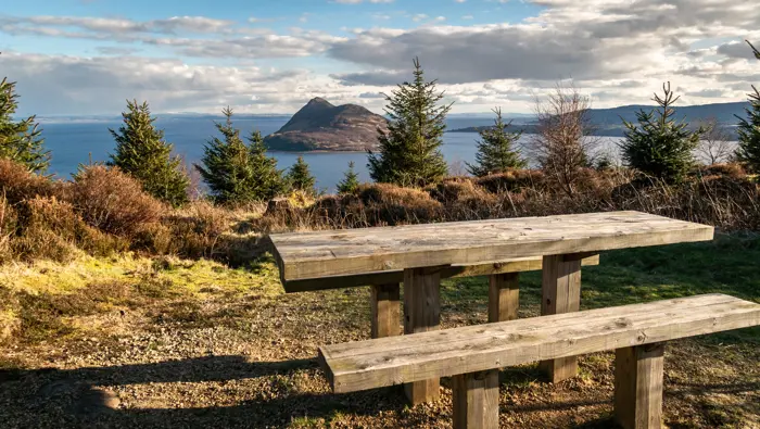 Picnic bench in the foreground with views to a small island out at sea.