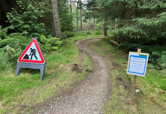 A section of trail with signage. One indicating that work is being done to it. The other indicating that the Trailfairies volunteers will be working there that day.