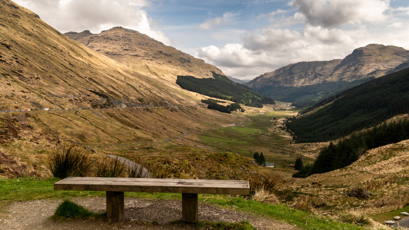 A bench on a hillside looking down a glen with trees