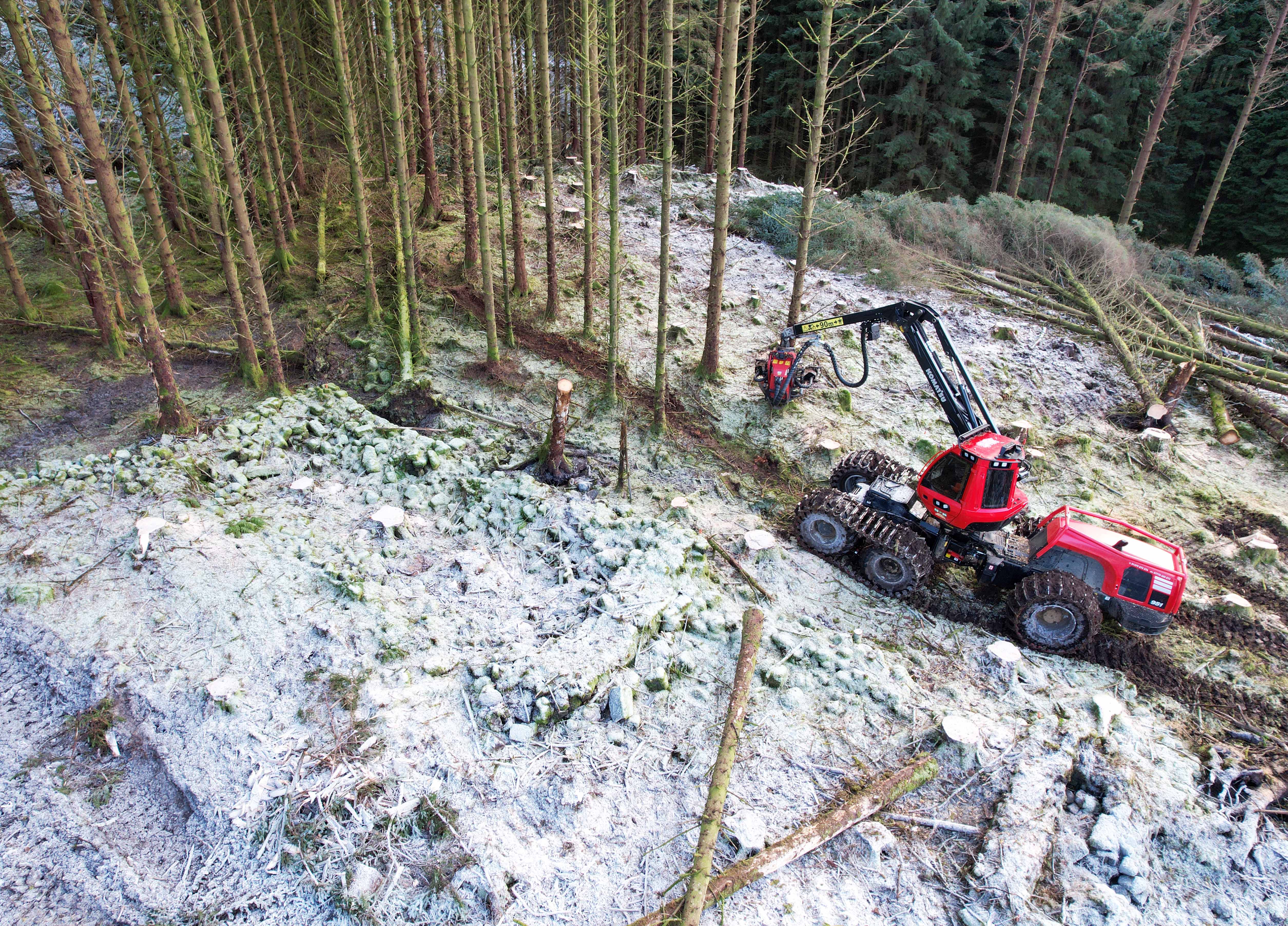A red harvesting machine removing trees with snow around it