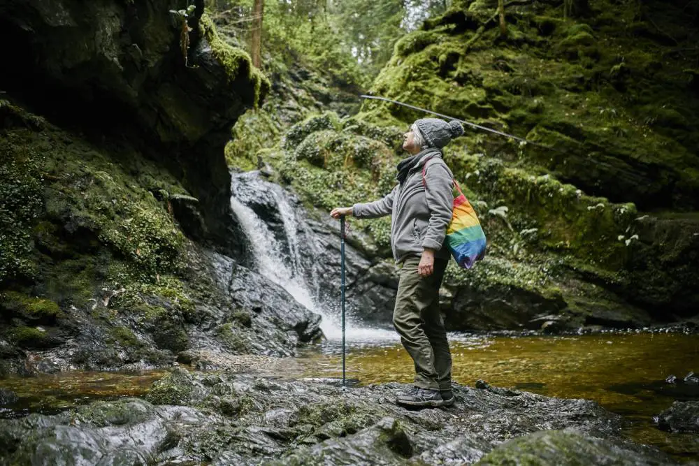 Man standing on rock next to waterfall and rocky pool