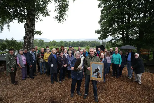 A man holds a portrait photo of an osprey in front of a large group