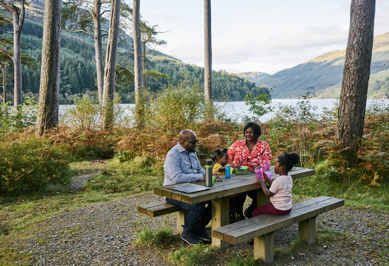 A family of four sit at a woodland picnic table